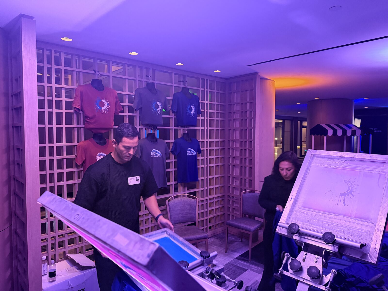 Wall of custom event shirts displayed behind a shirt bar